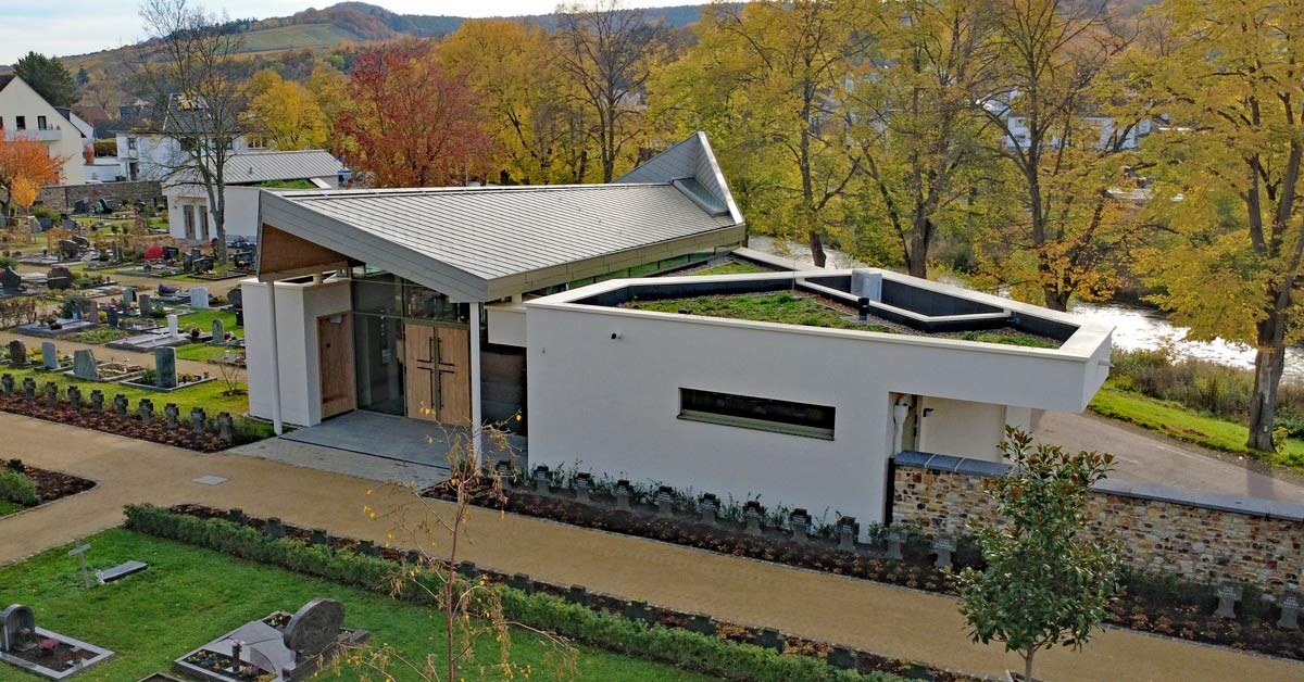 Die in Beigetönen gehaltene Aussegnungshalle öffnet sich über große Fensterflächen zum Licht – Symbol für den Übergang vom Irdischen zum Himmlischen. Ein Boden aus heimischer Grauwacke schafft Erdverbundenheit und Kontinuität.